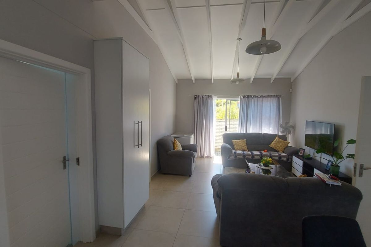 Spacious living room featuring vaulted ceilings with exposed rafters, tiled flooring, and a sliding glass door providing access to the outdoor area.