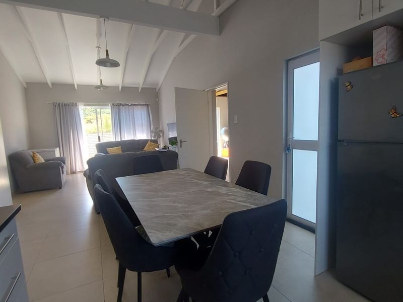 Spacious open-plan living and dining area featuring vaulted ceilings with exposed beams, tiled flooring, and direct access to the outdoor space.