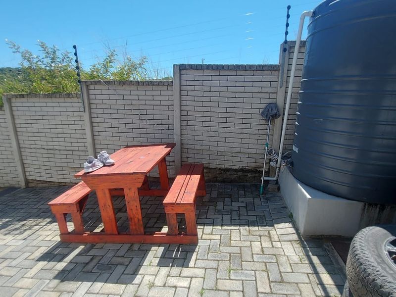 A paved rear courtyard area featuring a brick boundary wall with electric fencing and a large water storage tank.