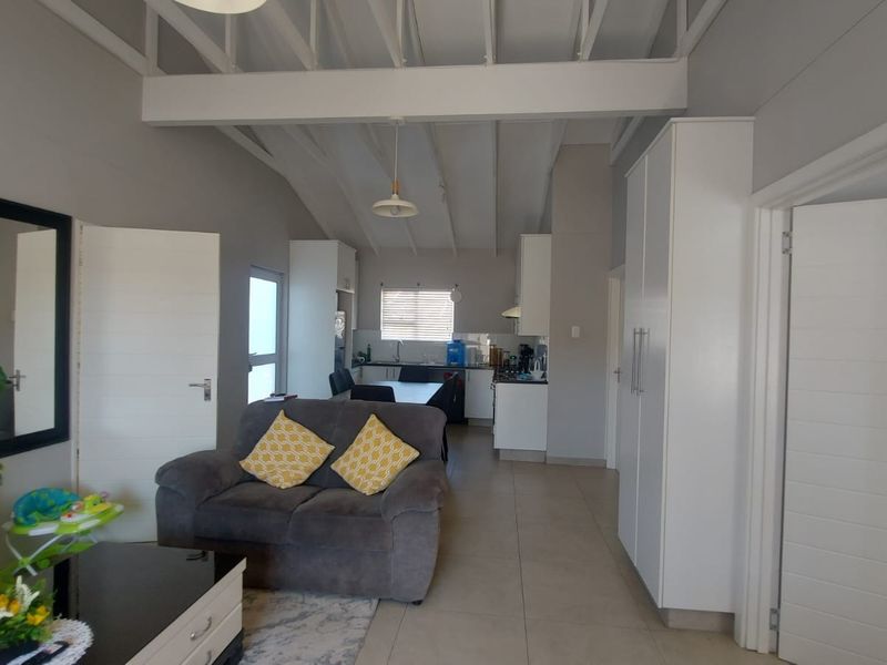 Open-plan living and kitchen area featuring vaulted ceilings with exposed rafters, tiled flooring, and modern built-in cabinetry.