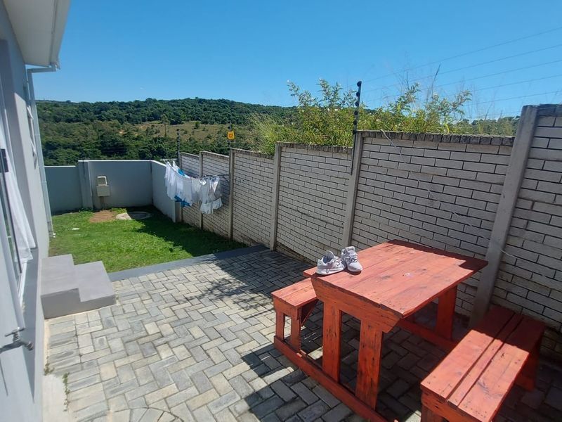 A private rear courtyard featuring a paved patio area, a small lawn, and secure brick boundary walls with electric fencing.