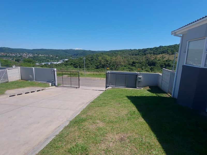 Front exterior view of the townhouse featuring a concrete driveway, secure sliding gate, perimeter wall with electric fencing, and scenic valley views.