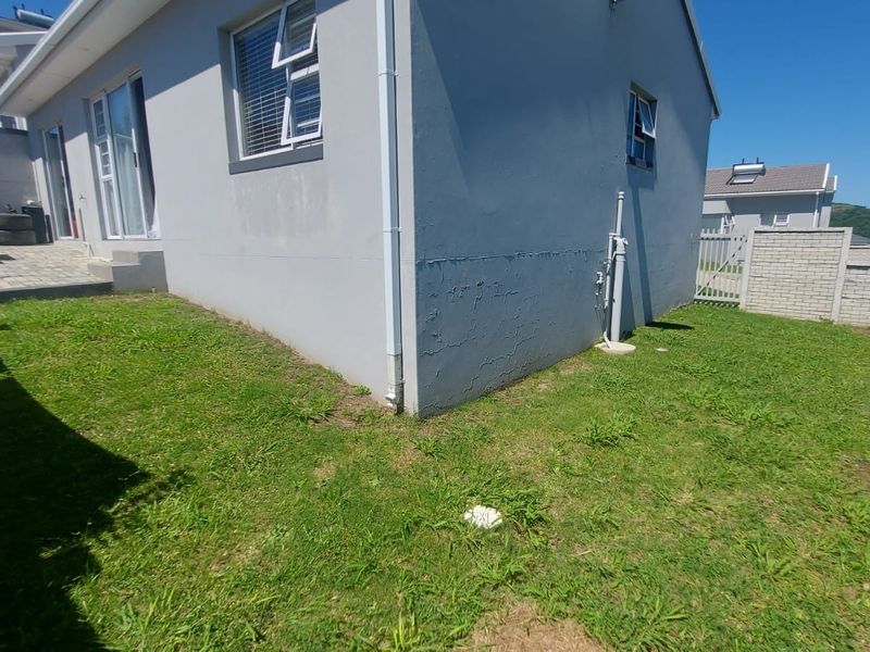 Rear view of the townhouse featuring a paved patio area, lawn, and boundary wall, with visible cracking on the exterior wall plaster.