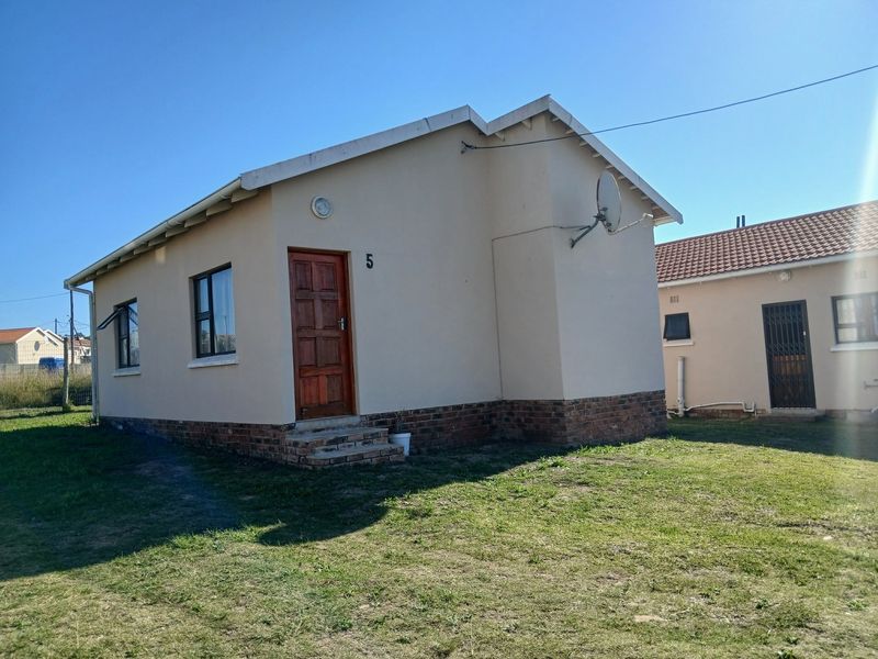 A detached single-story house featuring a neutral rendered facade, brick base, timber front door, and aluminium window frames set on a grassed plot.