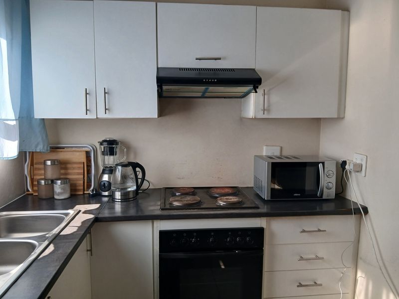 A functional kitchen featuring white cabinetry, a dark laminate countertop, a built-in oven, and an electric hob with an overhead extractor fan.