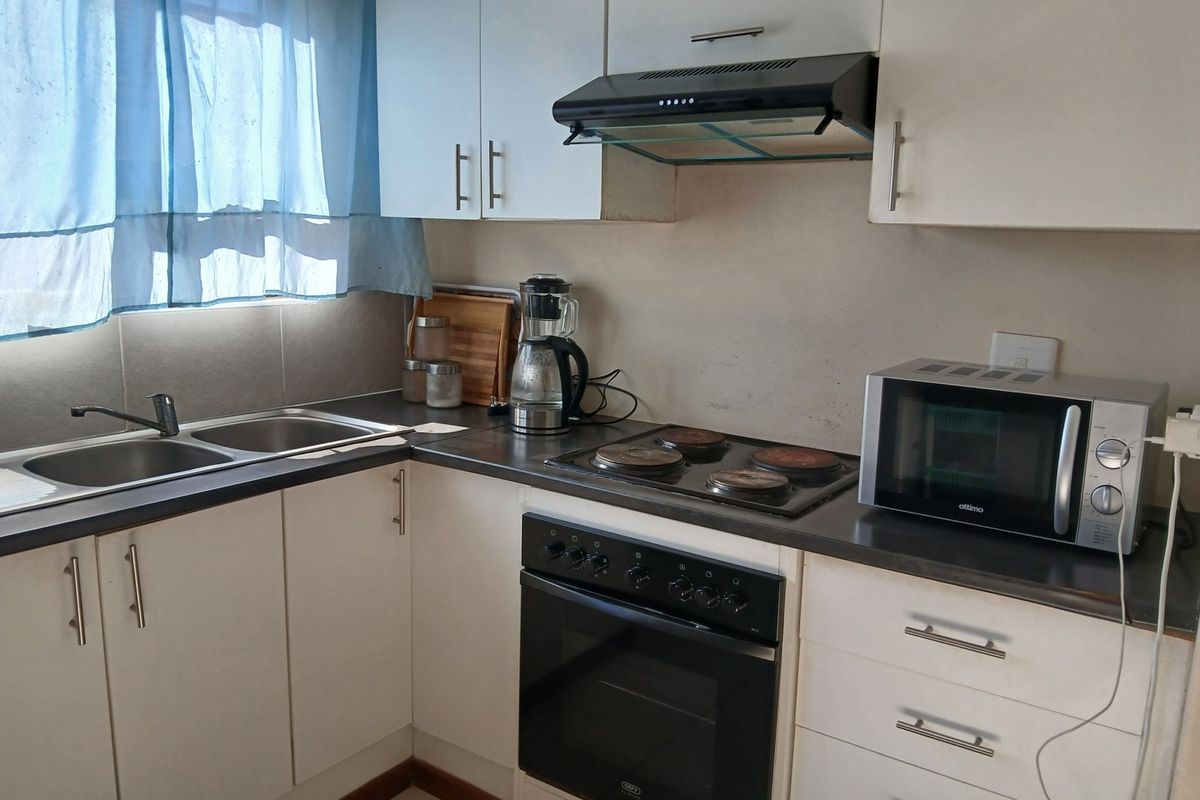A functional kitchen featuring white cabinetry, a double basin sink, built-in oven, electric hob, and extractor fan with laminate countertops.