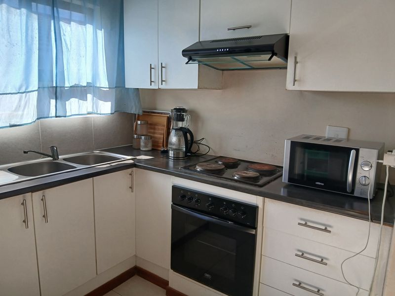 A functional kitchen featuring white cabinetry, a double basin sink, built-in oven, electric hob, and extractor fan with laminate countertops.