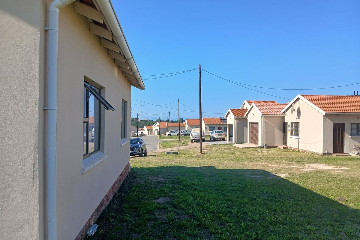 View of the rear exterior of the house showing the side facade, tiled roof, and surrounding residential neighborhood lawn area.