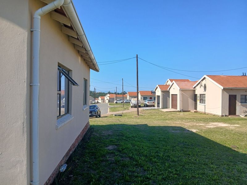 View of the rear exterior of the house showing the side facade, tiled roof, and surrounding residential neighborhood lawn area.
