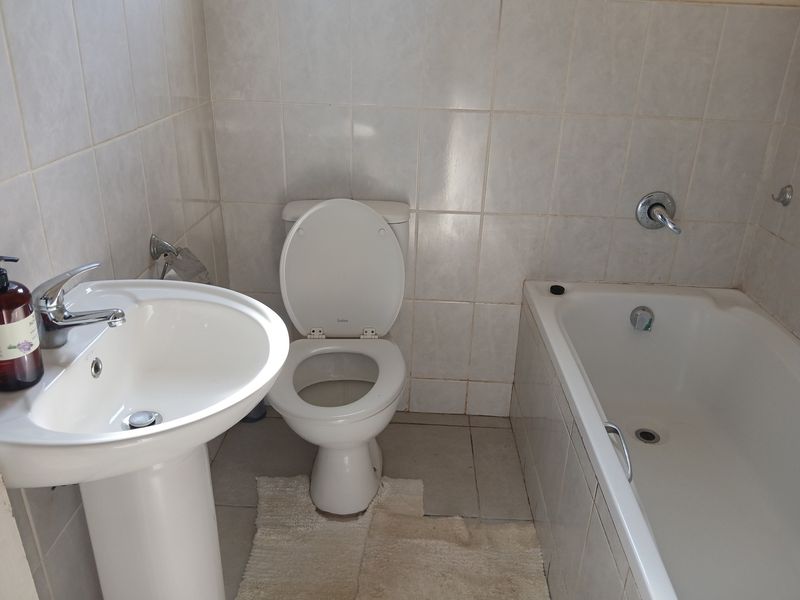 A functional bathroom featuring a pedestal basin, standard toilet, and a built-in bathtub with full-height wall tiling.