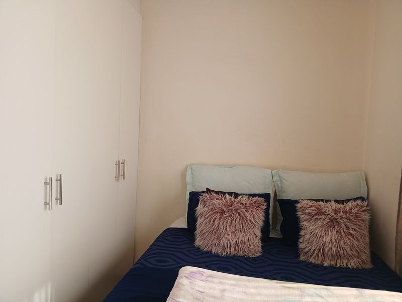 A compact bedroom featuring neutral walls and functional white built-in cupboards with modern handles.