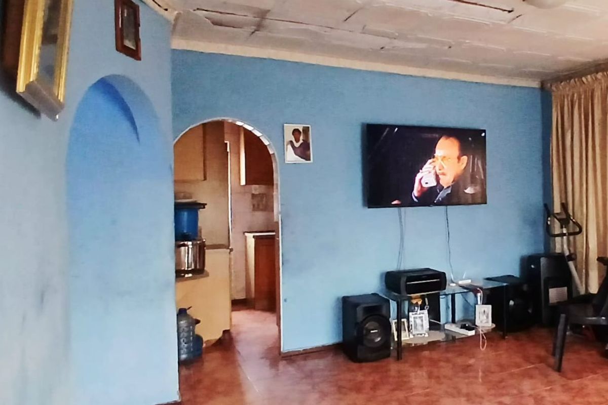 Living room featuring tiled flooring and an arched doorway leading to the kitchen area, with visible wear on the ceiling and walls.