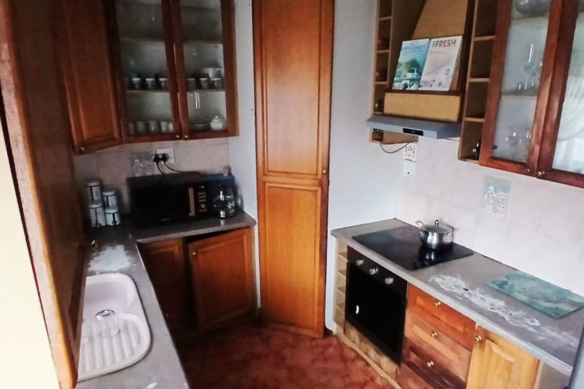 A functional kitchen featuring traditional wooden cabinetry, built-in oven and hob, extractor fan, and ample storage space with glass-fronted display units.