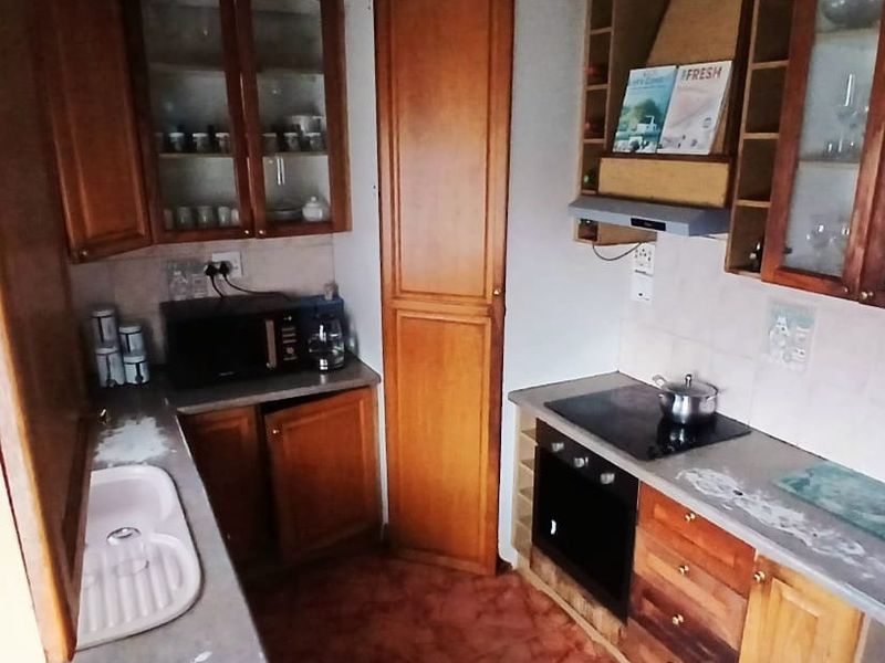 A functional kitchen featuring traditional wooden cabinetry, built-in oven and hob, extractor fan, and ample storage space with glass-fronted display units.
