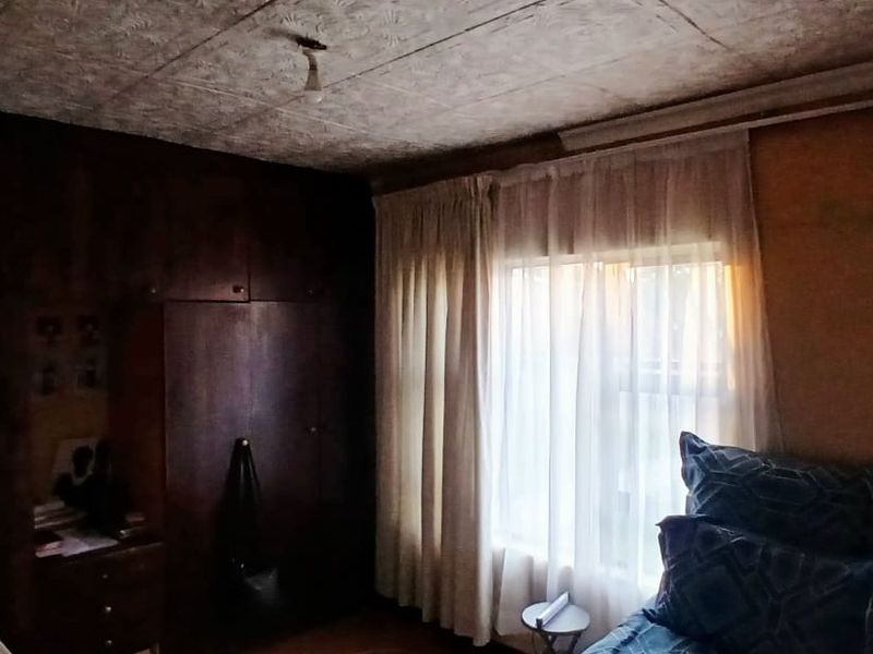 A bedroom featuring built-in wooden cupboards and a textured ceiling, requiring cosmetic updates to modernize the space.