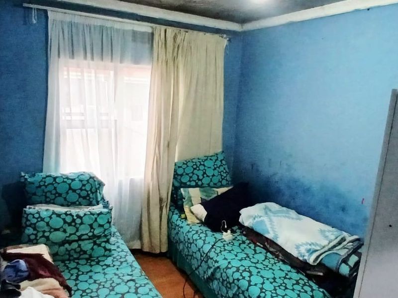 A compact bedroom featuring blue walls and a window with curtain rails, requiring cosmetic updates and wall repairs to improve the living space.