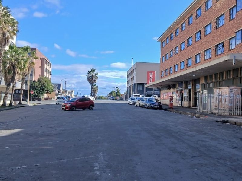 A street-level view of a commercial and residential area featuring brick buildings, paved roads, and surrounding urban infrastructure.