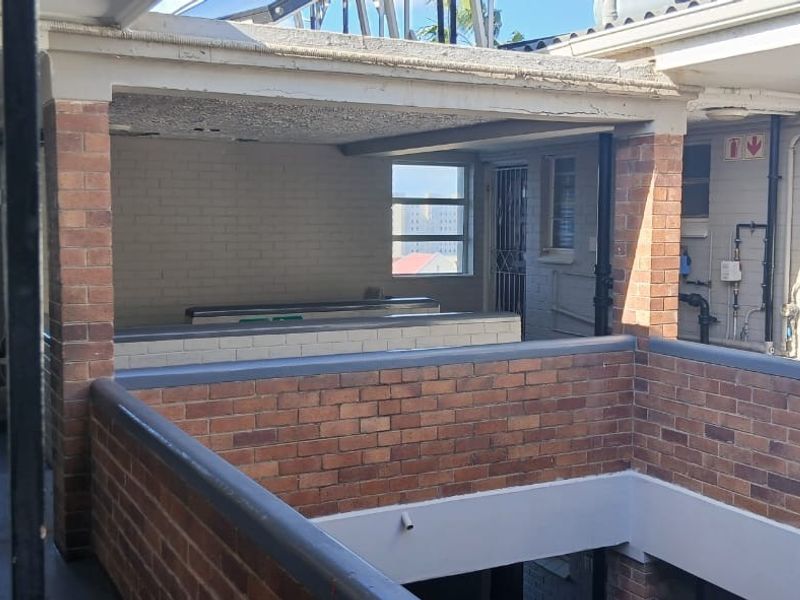 An open-air balcony or walkway area featuring exposed brickwork and structural beams, showing signs of wear and requiring maintenance.
