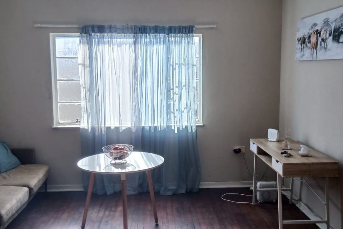 A living room featuring dark laminate flooring and a large window, providing a neutral base for interior design updates.