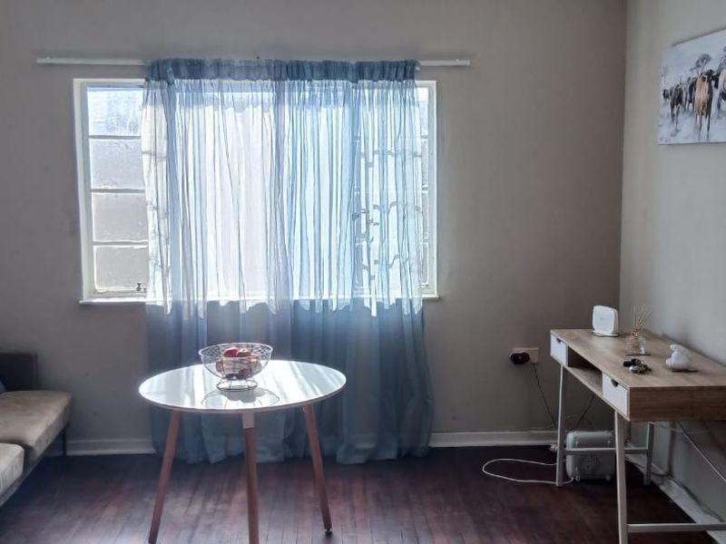 A living room featuring dark laminate flooring and a large window, providing a neutral base for interior design updates.