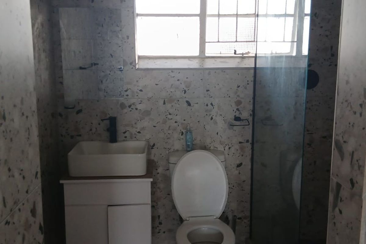 A bathroom featuring terrazzo wall tiles, a vessel sink with vanity cabinet, a toilet, and a glass shower screen.