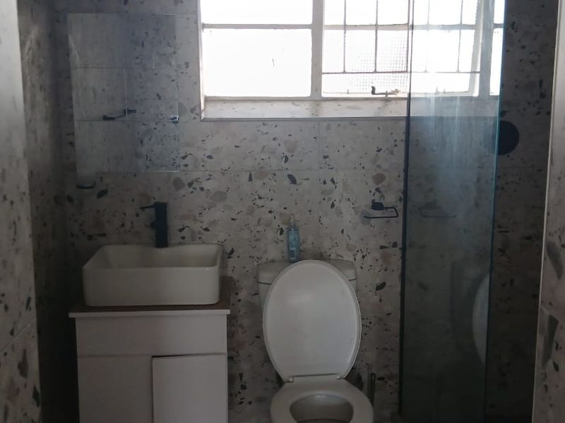 A bathroom featuring terrazzo wall tiles, a vessel sink with vanity cabinet, a toilet, and a glass shower screen.