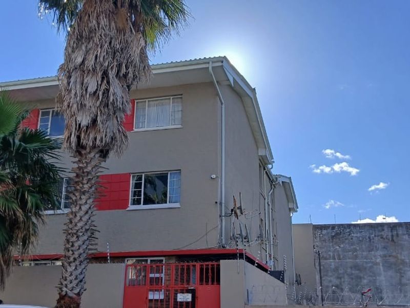 Exterior view of a multi-story residential building featuring a perimeter wall with electric fencing and metal gate access.