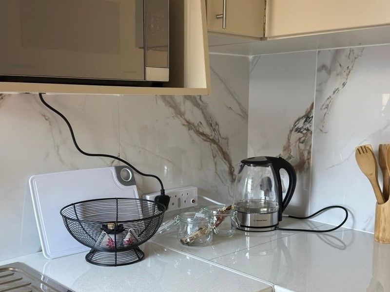 A clean kitchen corner featuring a built-in microwave, marble-effect splashback, and a functional countertop workspace.