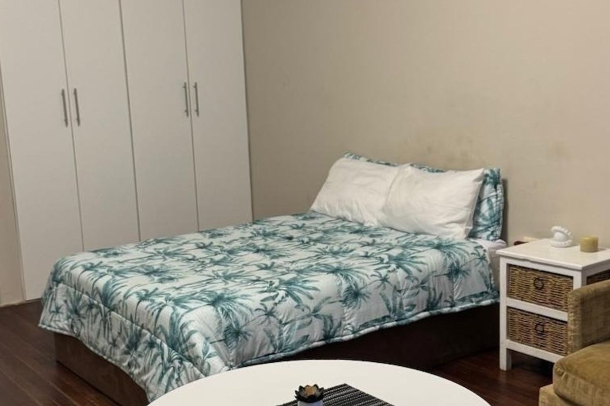 A bedroom featuring built-in cupboards and laminate flooring, with visible wall staining requiring attention.