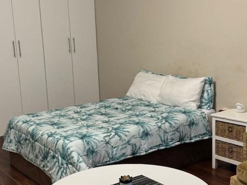 A bedroom featuring built-in cupboards and laminate flooring, with visible wall staining requiring attention.