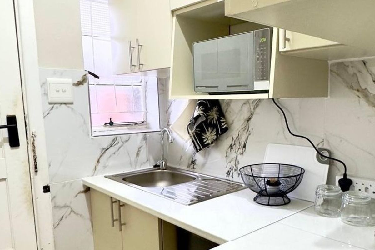A compact kitchen area featuring marble-look wall tiling, a stainless steel sink, and built-in cabinetry with an integrated microwave space.