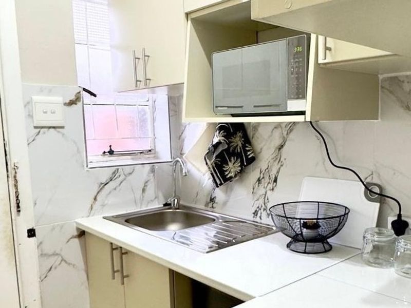 A compact kitchen area featuring marble-look wall tiling, a stainless steel sink, and built-in cabinetry with an integrated microwave space.