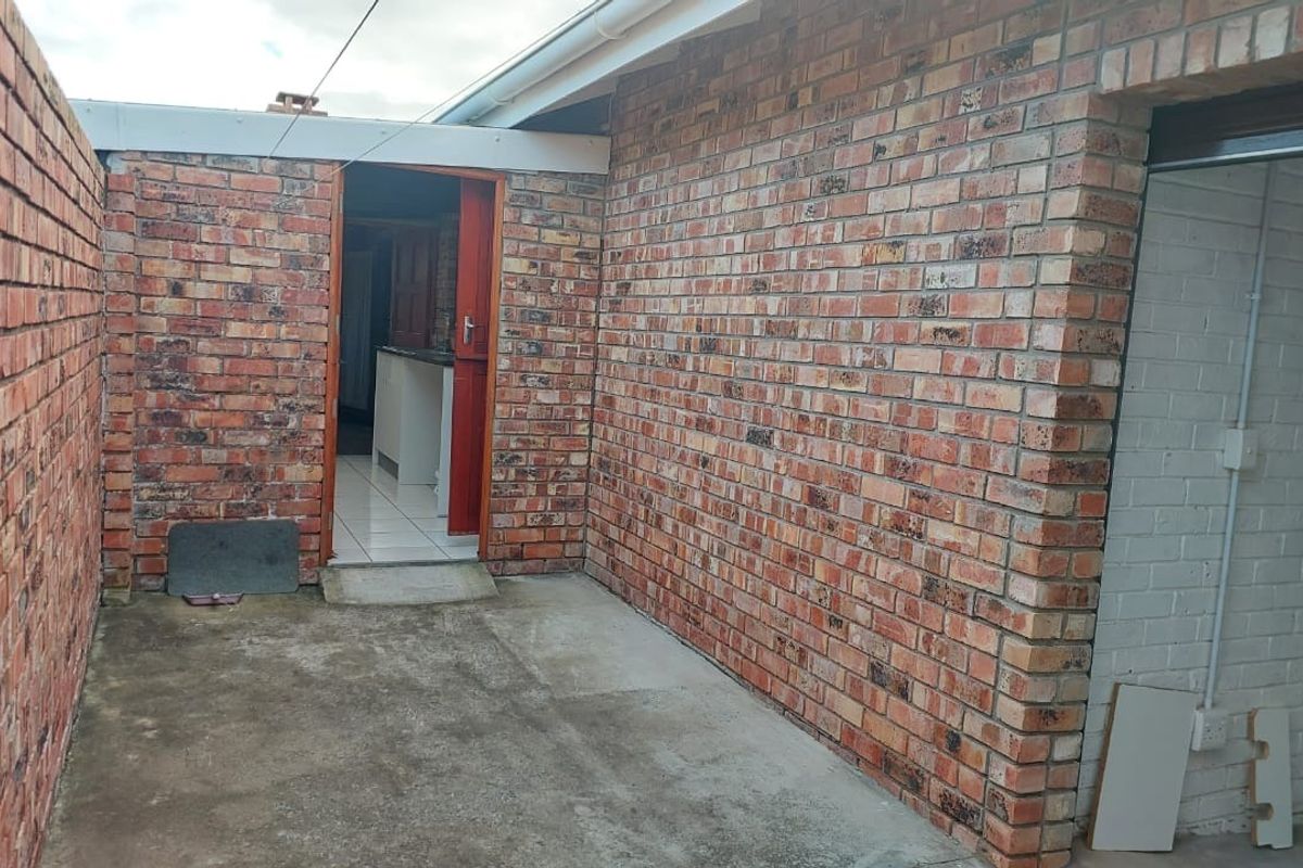 A rear exterior view of the townhouse featuring exposed brick walls, a concrete patio area, and an external access door.