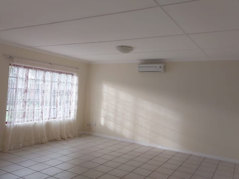 A spacious, empty living area featuring neutral tiled flooring, a wall-mounted split-system air conditioner, and a large window allowing natural light.
