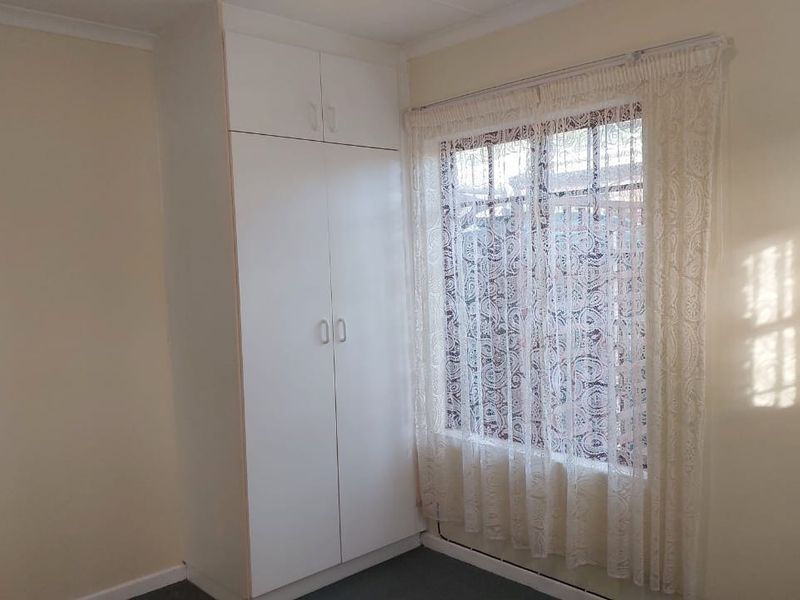 A clean, empty bedroom featuring a white built-in wardrobe and a window with security bars, providing a neutral space ready for personalization.