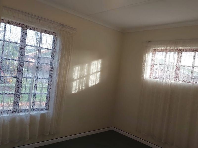 A bright, empty bedroom featuring dual aspect windows with security bars and neutral wall finishes, offering a blank canvas for personalization.