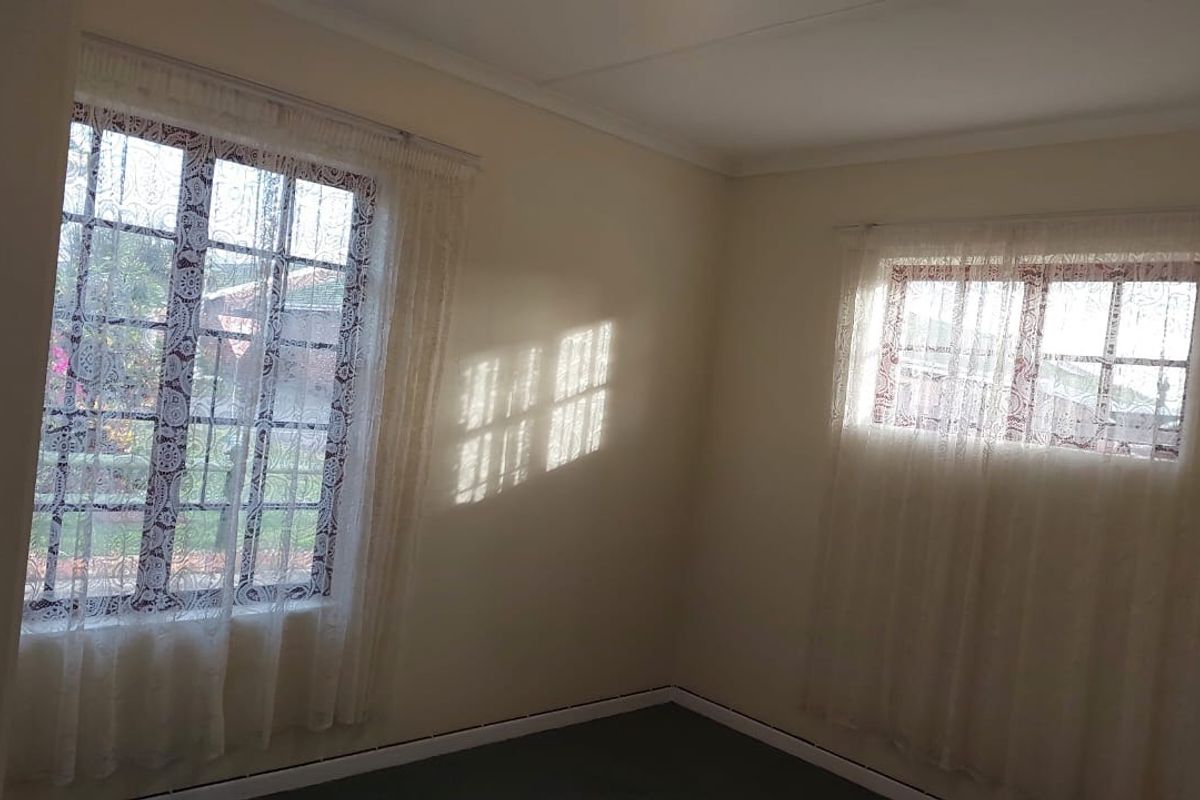 A bright, empty bedroom featuring dual aspect windows with security bars and neutral wall finishes, offering a blank canvas for personalization.