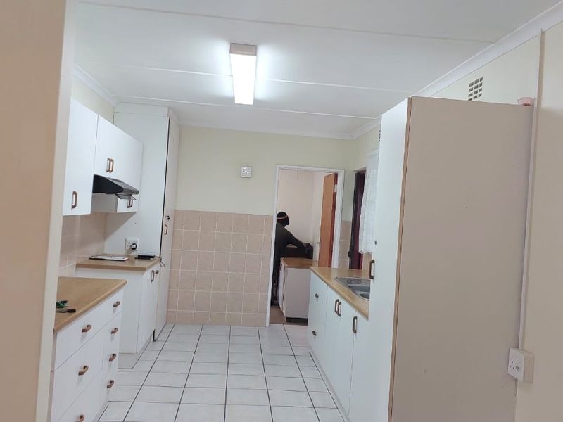 A functional, empty kitchen featuring white cabinetry, laminate countertops, tiled flooring, and a tiled splashback, offering a clean canvas for potential updates.