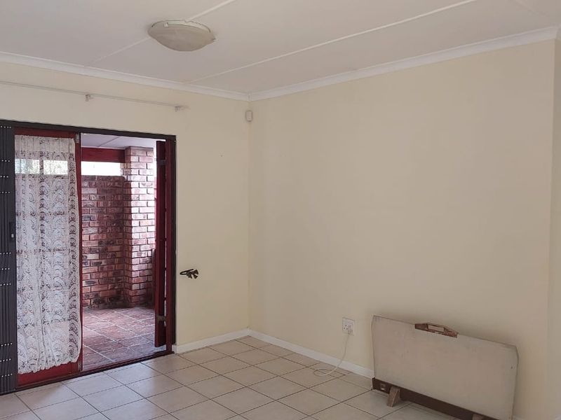 An empty living room featuring tiled flooring, a ceiling light fixture, and a sliding security gate leading to an outdoor patio area.