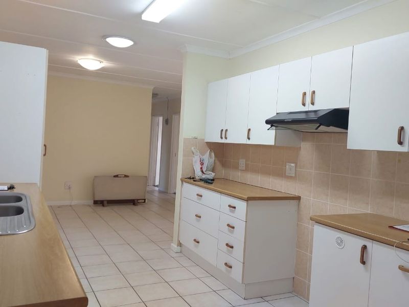 A functional kitchen featuring white cabinetry, laminate countertops, a double bowl sink, and tiled flooring, offering a clean and practical workspace.