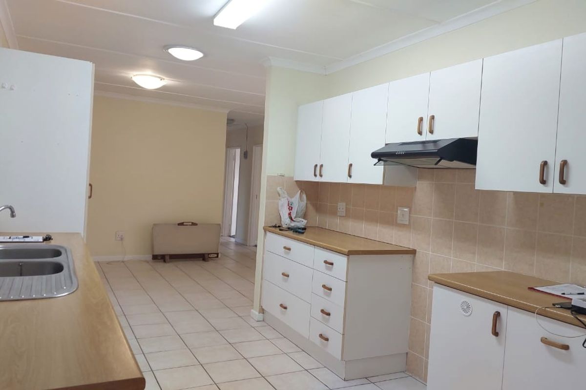 A functional kitchen featuring white cabinetry, laminate countertops, a double bowl sink, and tiled flooring, offering a clean and practical workspace.
