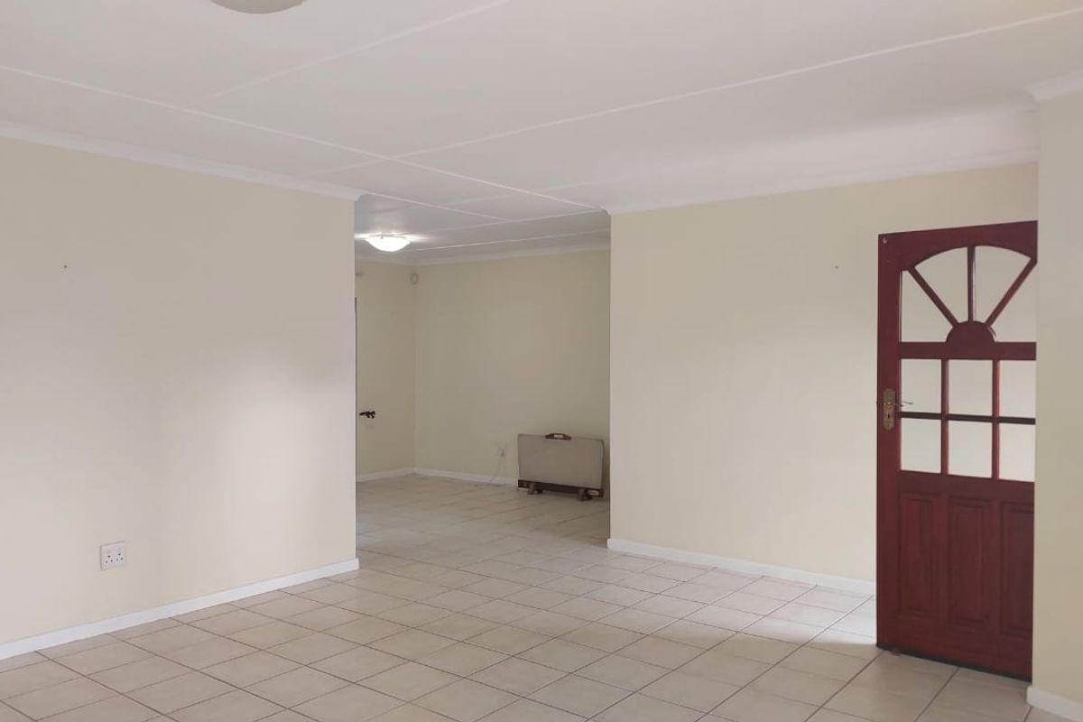 A spacious, vacant living area featuring neutral tiled flooring, coved ceilings, and a traditional timber panelled entrance door.