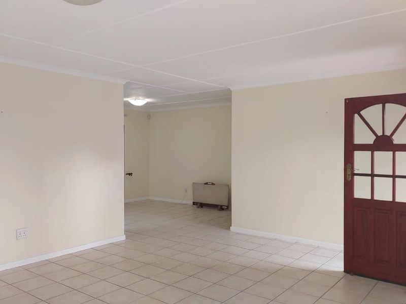 A spacious, vacant living area featuring neutral tiled flooring, coved ceilings, and a traditional timber panelled entrance door.