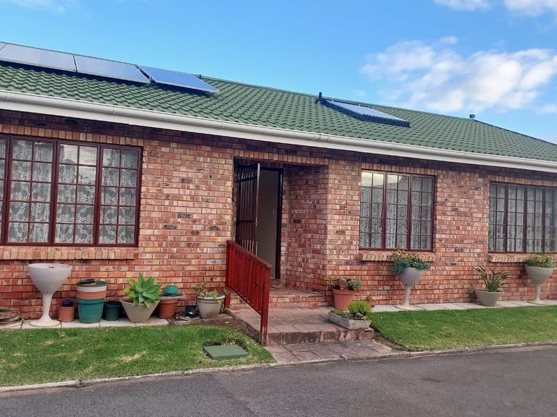 Front elevation of a face brick townhouse featuring a tiled roof, solar panels, solar geyser, and a paved entrance with security gate.