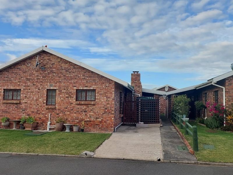 Front exterior view of a face brick townhouse featuring a concrete driveway, brick chimney, and established garden area.