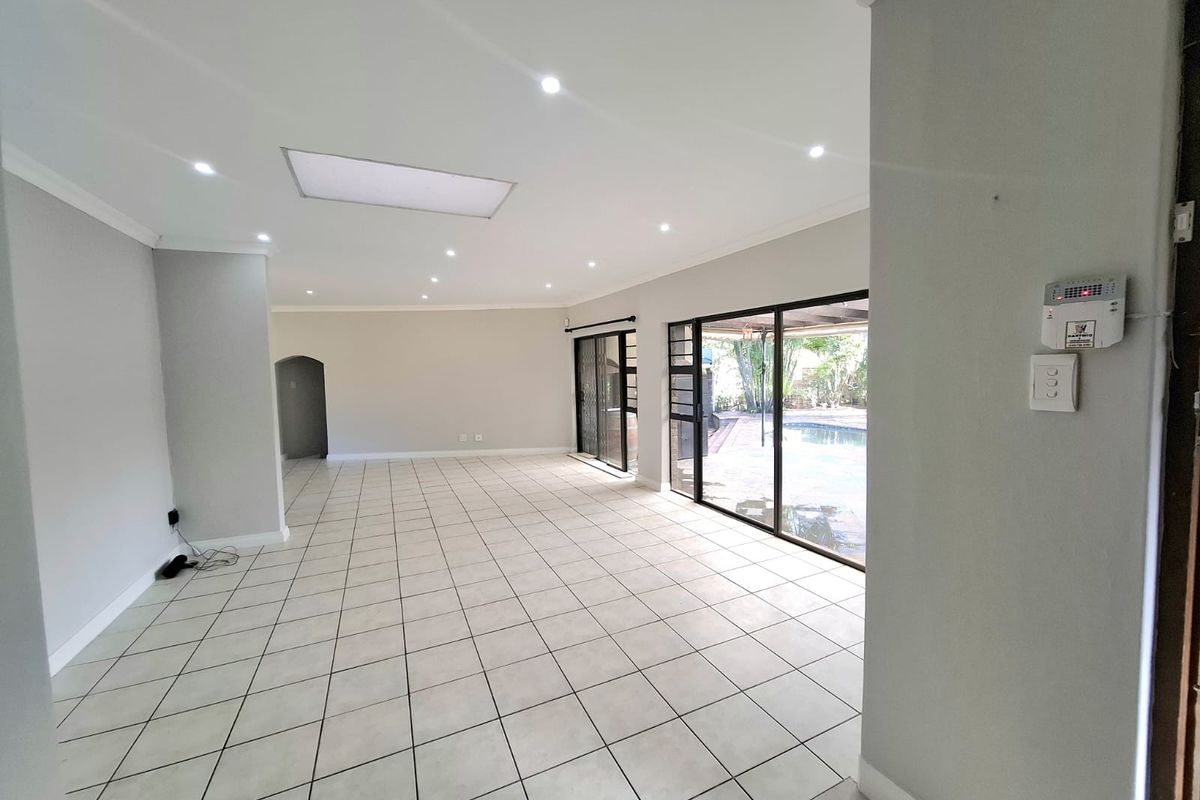 Spacious, open-plan living area featuring neutral tiled flooring, recessed lighting, and large sliding glass doors providing direct access to the outdoor pool area.