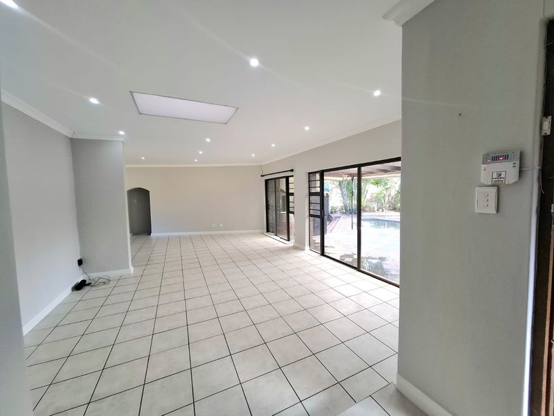 Spacious, open-plan living area featuring neutral tiled flooring, recessed lighting, and large sliding glass doors providing direct access to the outdoor pool area.