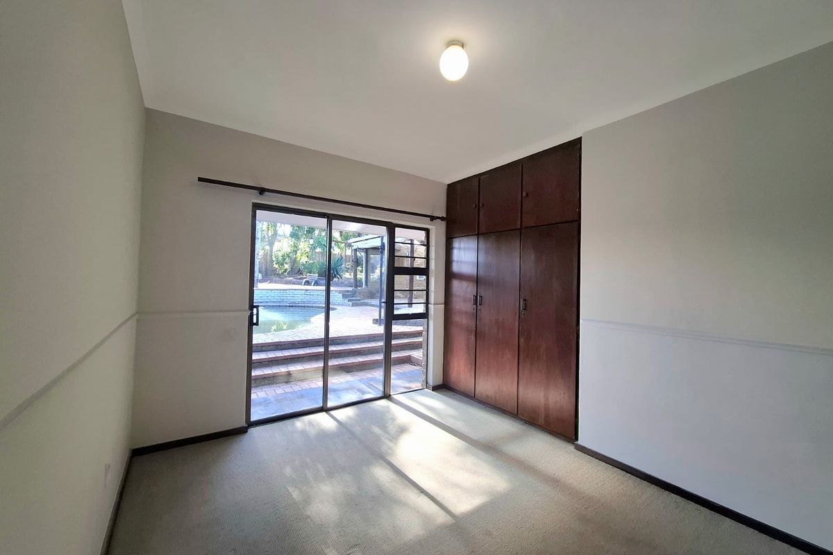 A spacious, empty bedroom featuring built-in wooden cupboards, carpeted flooring, and a sliding glass door providing direct access to the outdoor pool area.