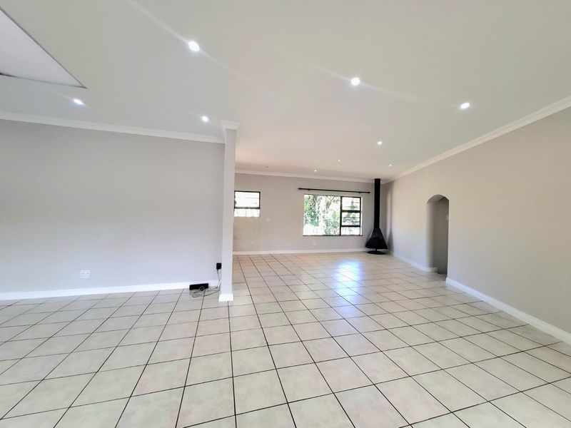 Spacious open-plan living area featuring neutral tiled flooring, recessed downlights, and a modern freestanding fireplace, offering a versatile and bright blank canvas.