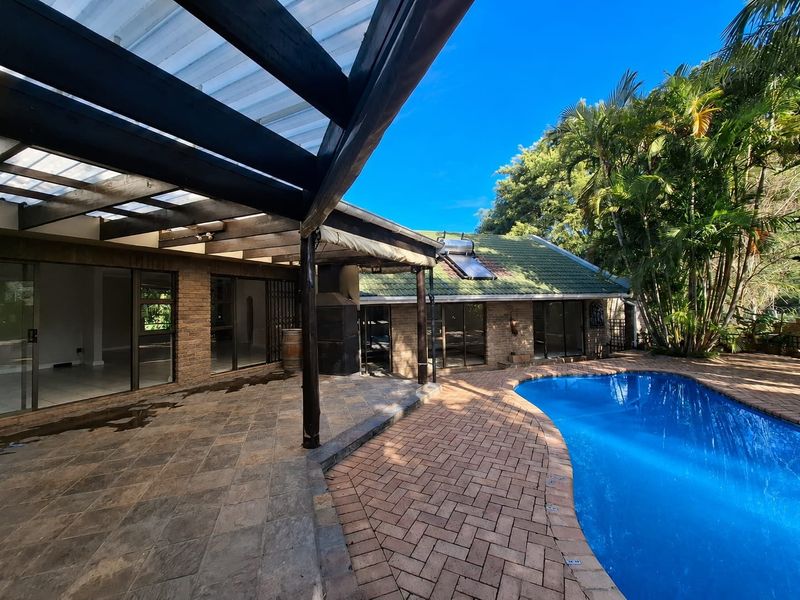 Outdoor entertainment area featuring a swimming pool, paved surround, and a covered patio with a timber pergola and built-in braai.